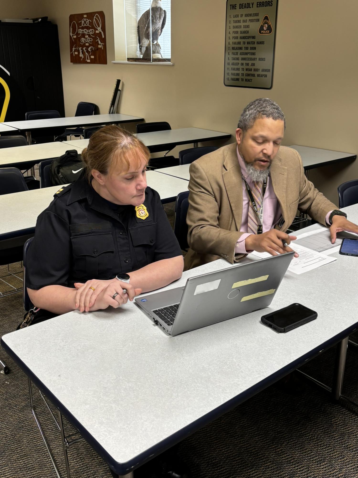 a woman officer works with a man in a suit on a laptop at a desk